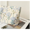 A floral canvas makeup bag featuring blue and green botanical embroidery resting on a white surface.