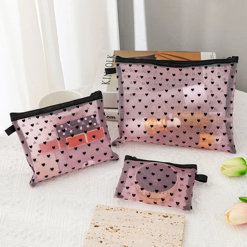 A collection of portable mesh cosmetic storage pouches in pink and black patterns displayed on a white surface.