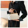 A woman holds a cream pearl embellished crossbody shoulder bag against a dark sweater.
