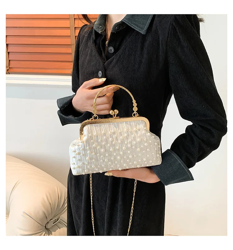 A woman holds a cream pearl embellished crossbody shoulder bag against a dark sweater.