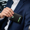 A hand is holding a black bi-fold leather wallet with a green accent, partially inside a navy blue suit jacket.