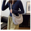 A woman holds a light gray canvas crossbody bag with a dark blue blazer and olive green trousers.