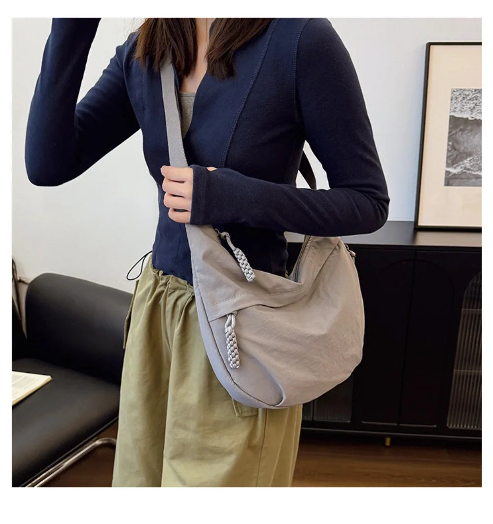 A woman holds a light gray canvas crossbody bag with a dark blue blazer and olive green trousers.