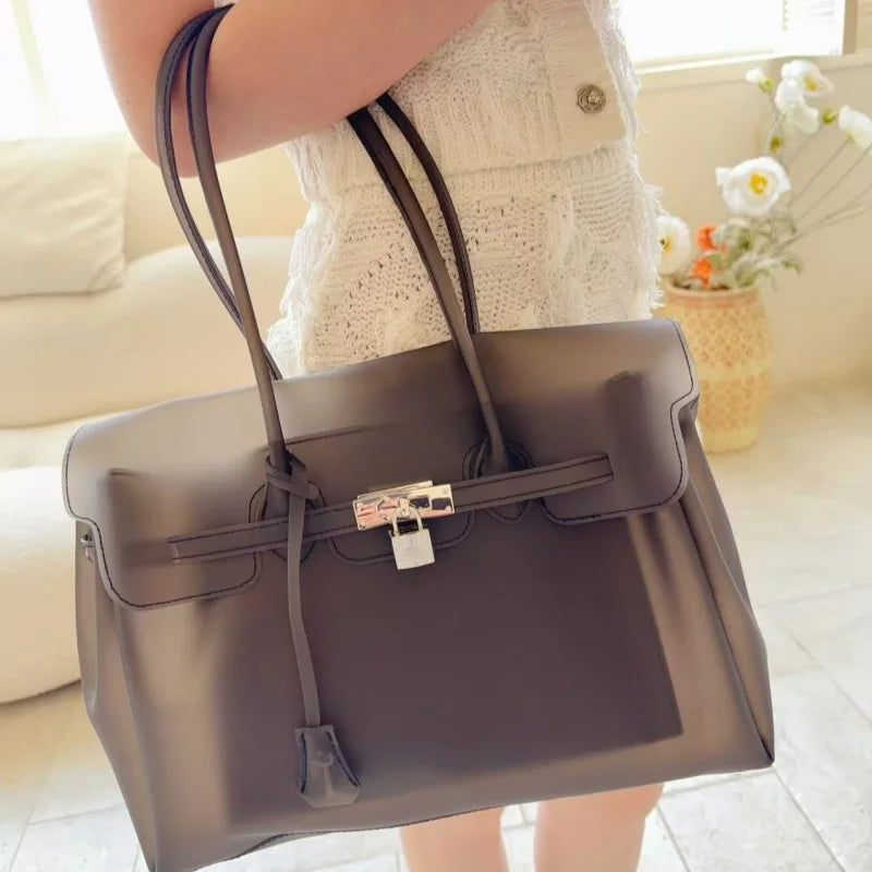Eine Frau hält eine graue Leder-Sommer-Jelly-Schultertasche in einem hellen Innenraum.