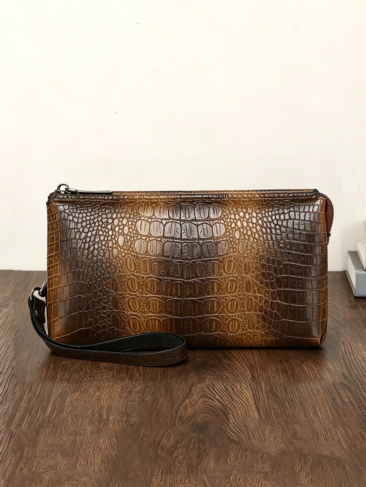 Clutch de estampado de cocodrilo marrón sobre una superficie de madera oscura.