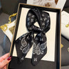 A black paisley silk hair scarf tied in a bow displayed in a black frame.