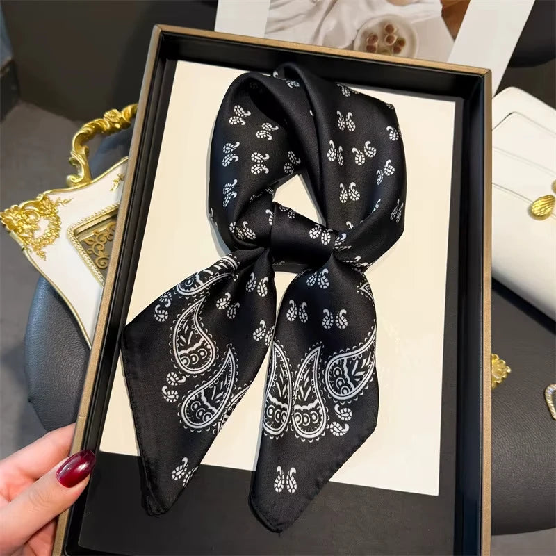 A black paisley silk hair scarf tied in a bow displayed in a black frame.