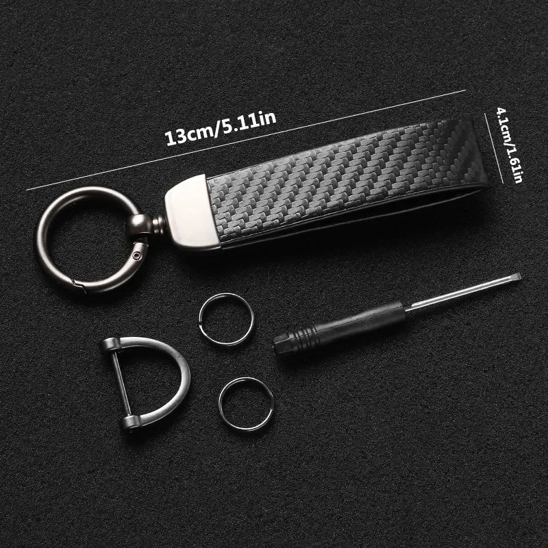 A black carbon fiber leather keychain with a silver ring and a small metal tool.