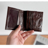A close-up of a dark brown genuine leather bifold wallet being held by a hand.
