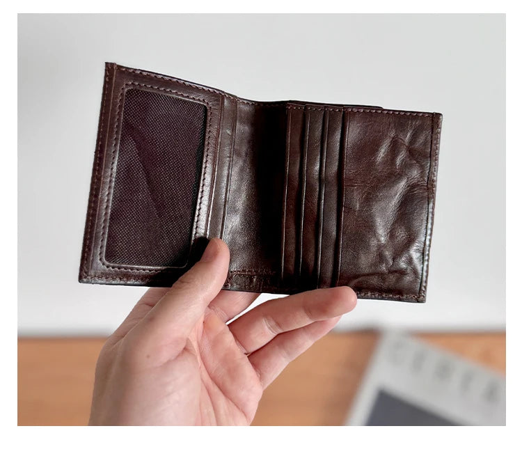 A close-up of a dark brown genuine leather bifold wallet being held by a hand.