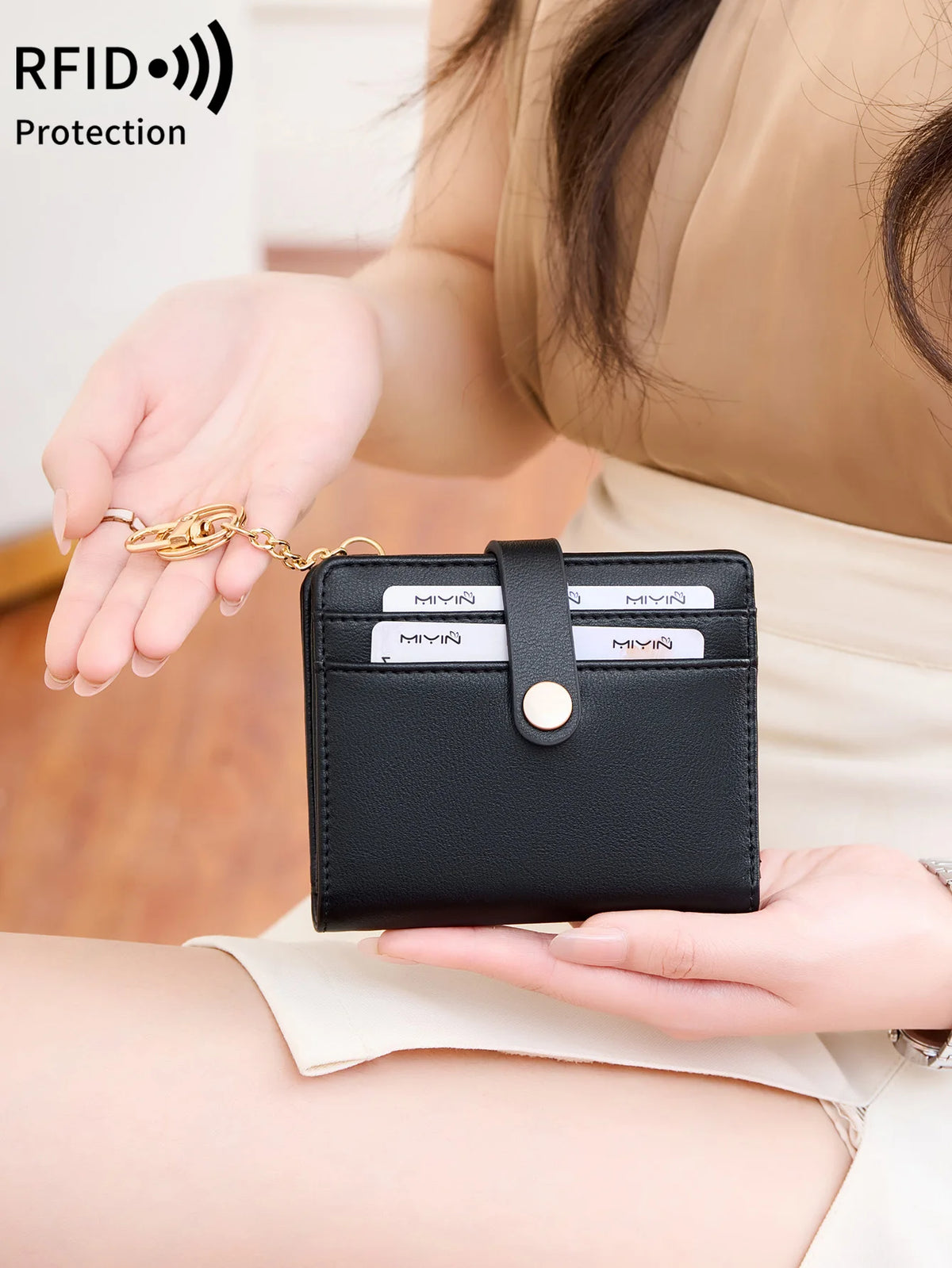 A hand holds a black minimalist RFID blocking wallet with a gold chain, demonstrating card protection.