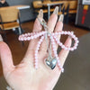 A hand holds a pink pearl keychain with a heart charm and silver chain.