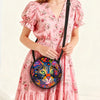 A woman wearing a pink floral dress carrying a round, colorful cartoon cat crossbody bag.