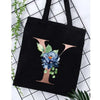 Black canvas tote bag featuring a large gold letter Y and blue floral print against a white background.