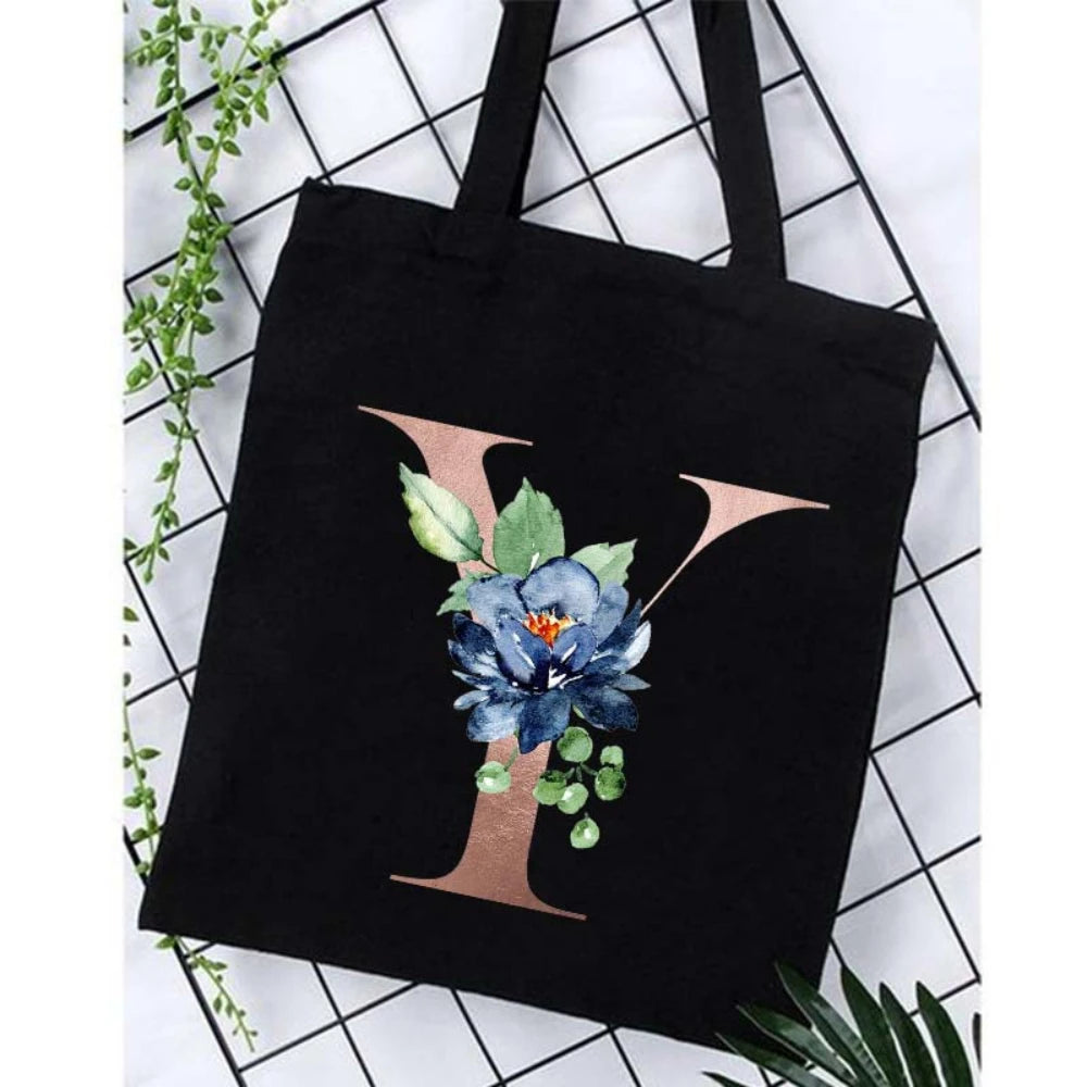 Black canvas tote bag featuring a large gold letter Y and blue floral print against a white background.
