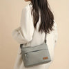 A light gray nylon crossbody shoulder bag with a leather tag is carried by a person wearing a cream-colored coat.