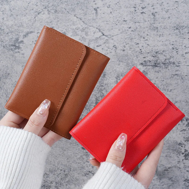 A hand holds a brown leather card wallet and a red leather card wallet against a gray background.
