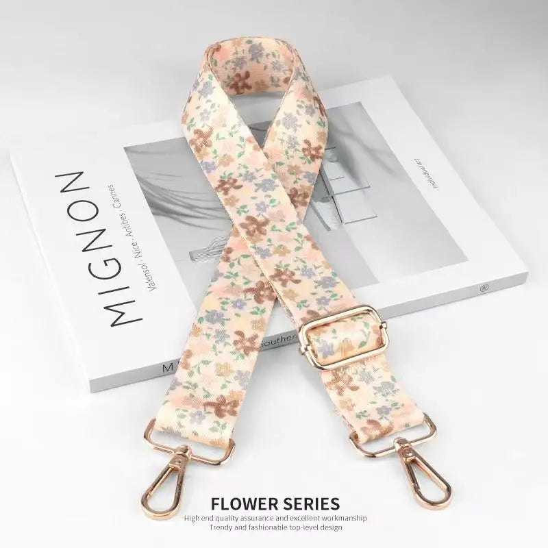 A beige floral patterned nylon bag strap with gold hardware displayed on a white box.
