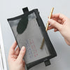 A hand holds a clear mesh zipper pouch with a black exterior and a gold pen inside.