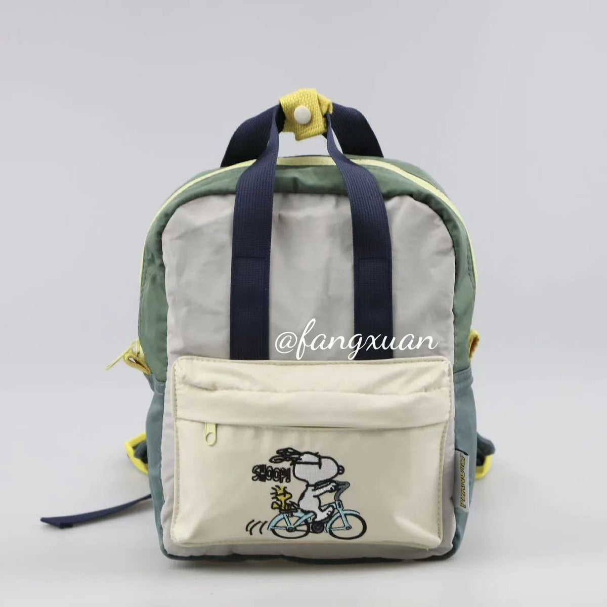 A light gray canvas shoulder bag featuring a Snoopy cartoon design and dark blue straps.