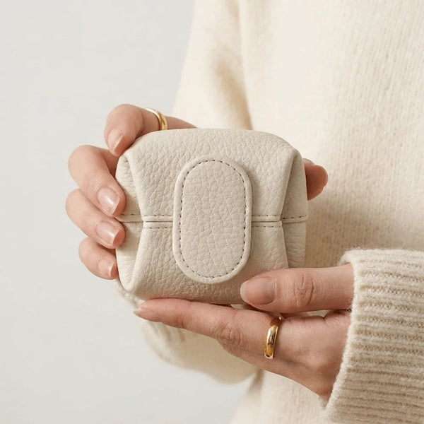 A hand holds a beige lychee-textured coin purse with a snap closure against a light background.