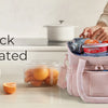 A pink insulated lunch bag is shown next to fresh fruit on a light countertop.