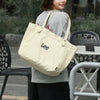 A woman wearing a grey top and black skirt holds a beige Korean style Oxford cloth tote bag.