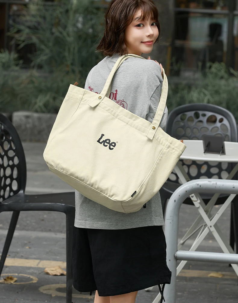 A woman wearing a grey top and black skirt holds a beige Korean style Oxford cloth tote bag.
