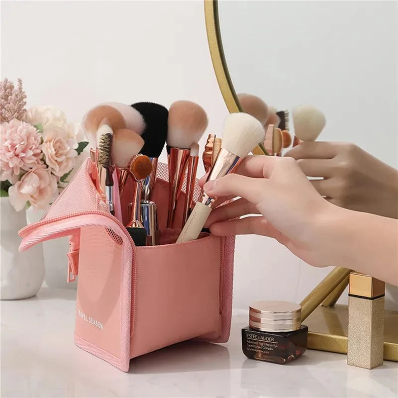 A pink foldable makeup brush storage case with various makeup brushes is shown on a white surface.