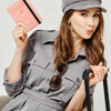 A woman wearing a gray uniform shirt holds a pink passport and sunglasses.