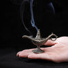 Antique metal incense burner with smoke rising, held in a hand against a dark background.