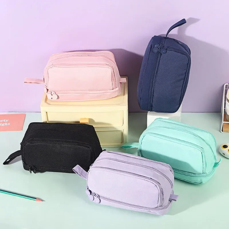 A collection of pink, blue, and purple multifunctional pencil cases for students displayed on a light green surface.