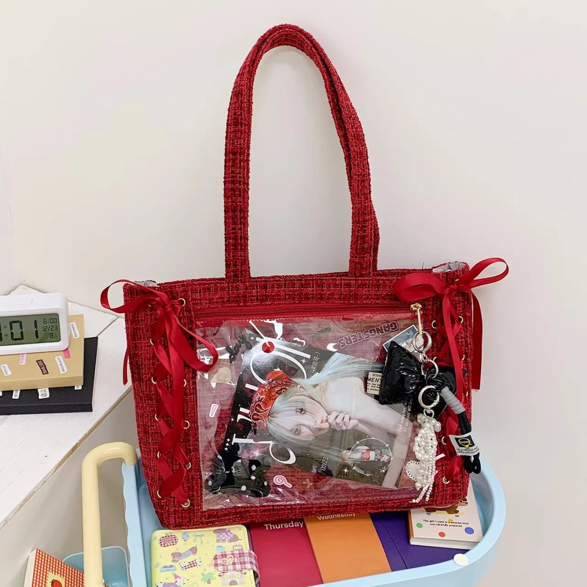 A red woven shoulder tote bag with a transparent front featuring a collage of accessories and items.