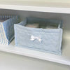 Light blue quilted cotton storage basket with a white lace flower design sitting on a white shelf.