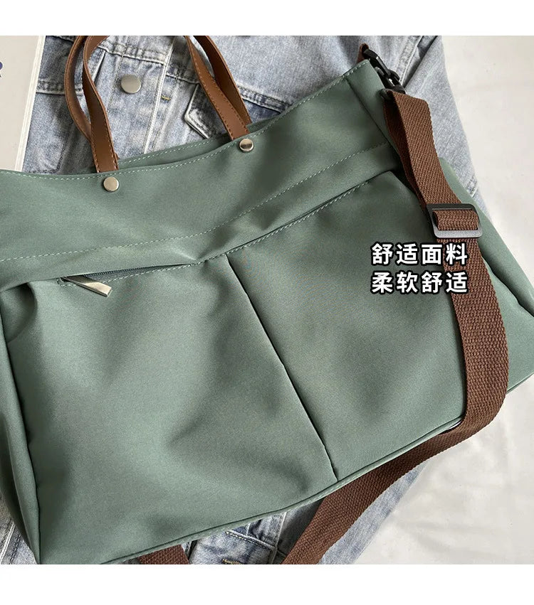 A light sage green nylon tote bag with brown straps and multiple internal pockets shown against a denim background.