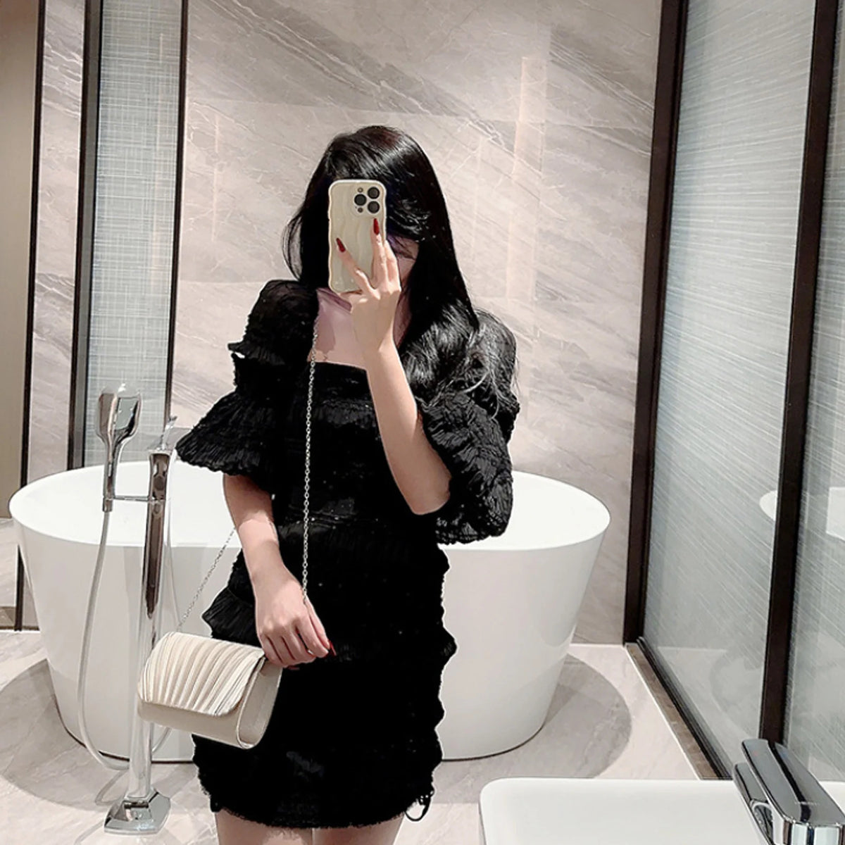 A woman holds a black luxury chain shoulder clutch bag in a stylish indoor setting.