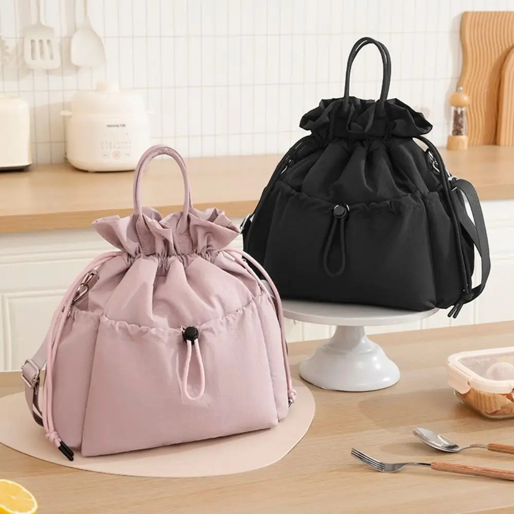 A pink insulated waterproof lunch bag with a drawstring is displayed on a wooden table.