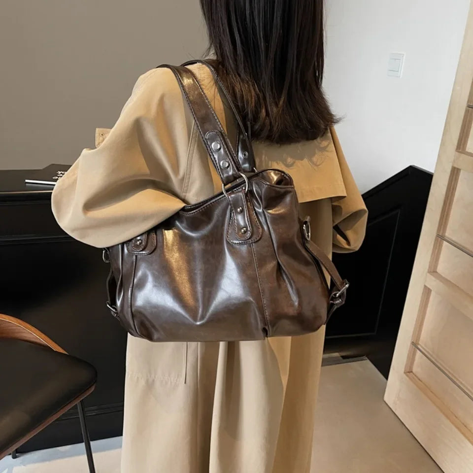 A woman wearing a beige tunic holds a brown leather tote bag with a strap.