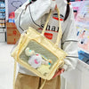 A light yellow transparent mesh shoulder tote bag with a white fluffy bear charm carried by a person.