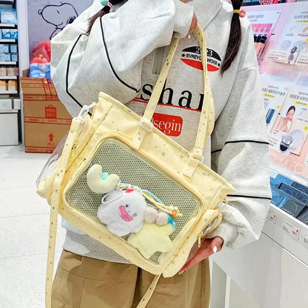 A light yellow transparent mesh shoulder tote bag with a white fluffy bear charm carried by a person.