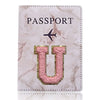 Una funda de pasaporte de imitación de cuero rosa claro con la palabra PASAPORTE y una gran letra U dorada grabada.