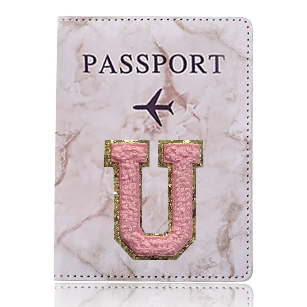 Una funda de pasaporte de imitación de cuero rosa claro con la palabra PASAPORTE y una gran letra U dorada grabada.