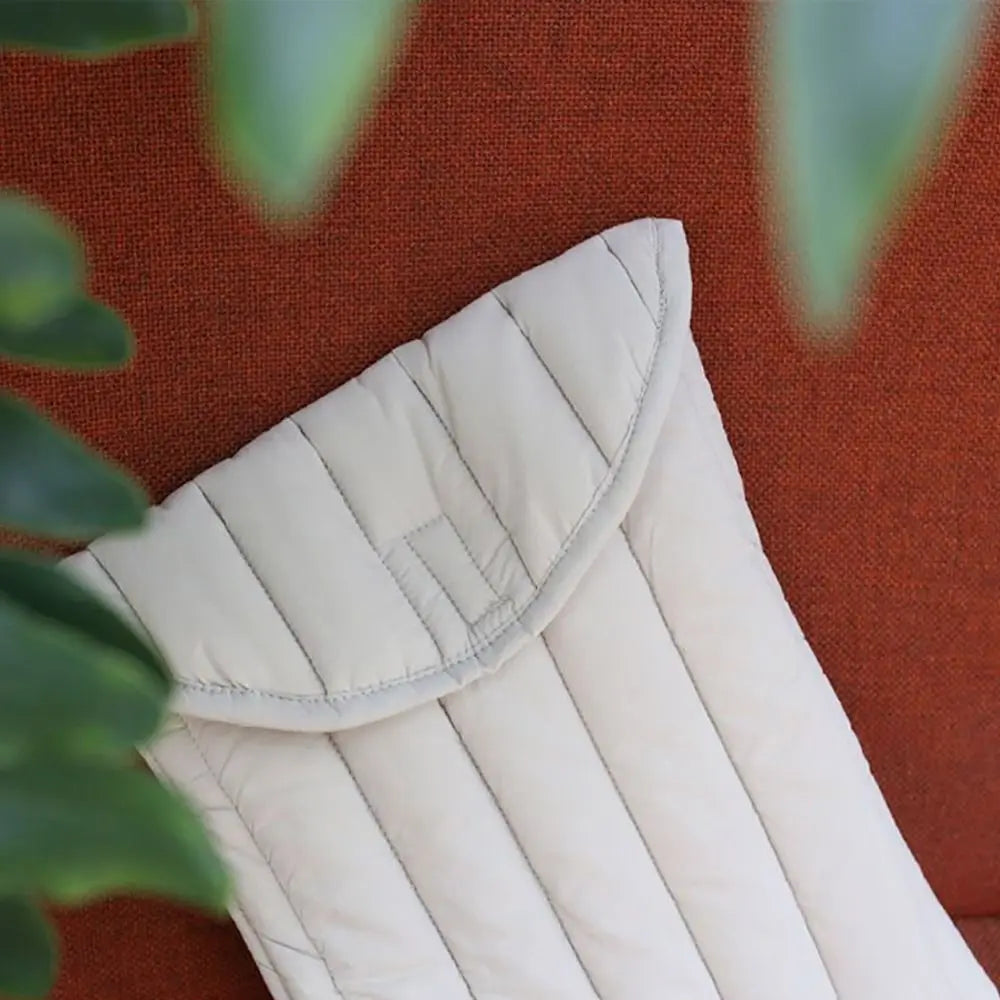 A cream-colored embroidered cotton laptop sleeve resting on a reddish-brown surface with green foliage in the foreground.