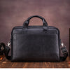 A black genuine leather men's briefcase with padded straps resting on a wooden surface.