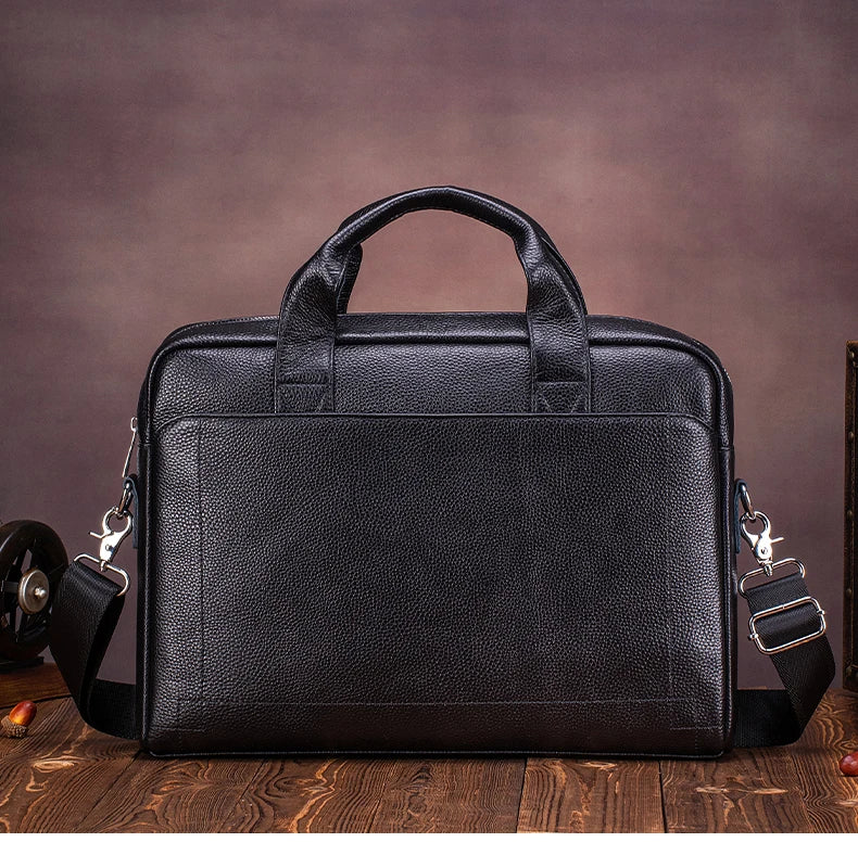 A black genuine leather men's briefcase with padded straps resting on a wooden surface.