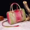 A luxury crocodile pattern crossbody tote bag in red and lime green leather rests on a light surface next to a piece of drift