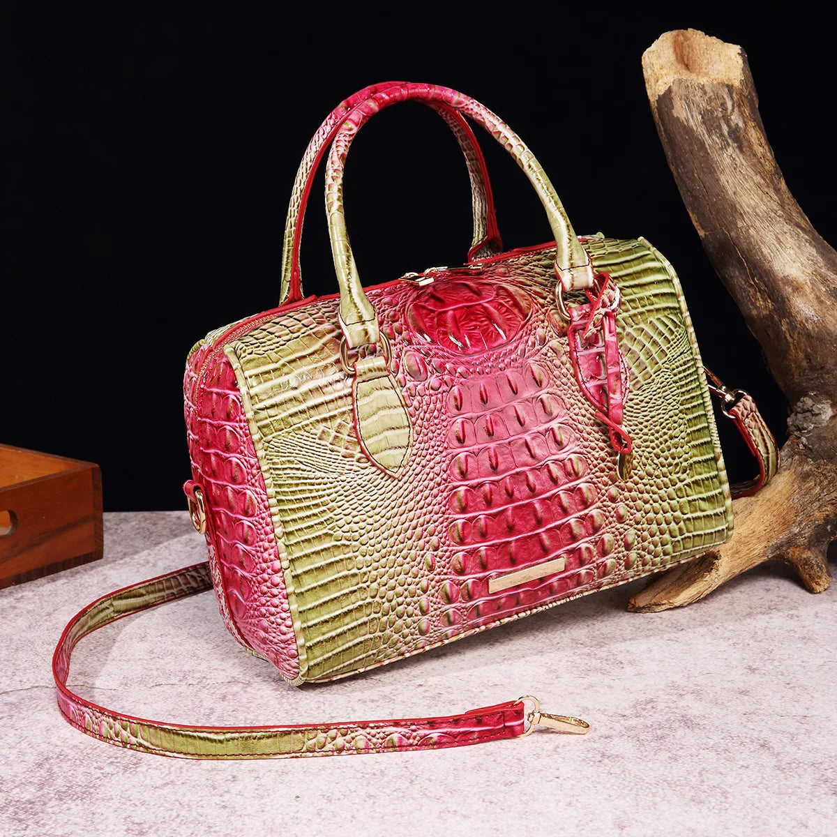 A luxury crocodile pattern crossbody tote bag in red and lime green leather rests on a light surface next to a piece of drift