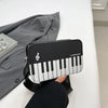 A black and white musical note embroidery crossbody bag with a piano print resting on a white surface.
