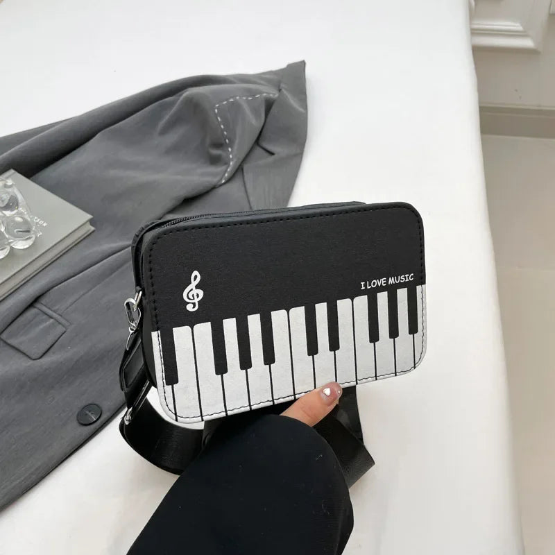 A black and white musical note embroidery crossbody bag with a piano print resting on a white surface.