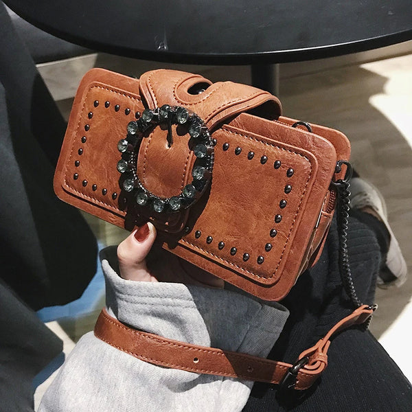 A brown vintage PU leather crossbody bag with a rhinestone buckle is being held by a person.